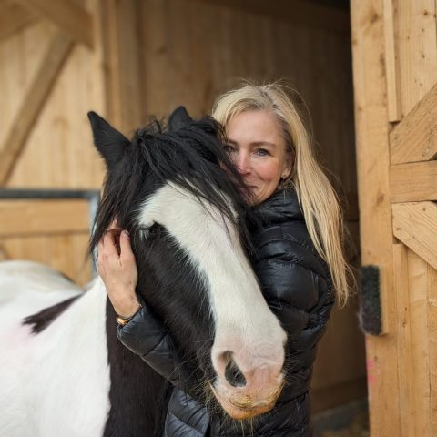 Reittherapeutin Gudrun Marquardt-Teuscher mit der Tinkerstute Lotti vor einem Holzstall.