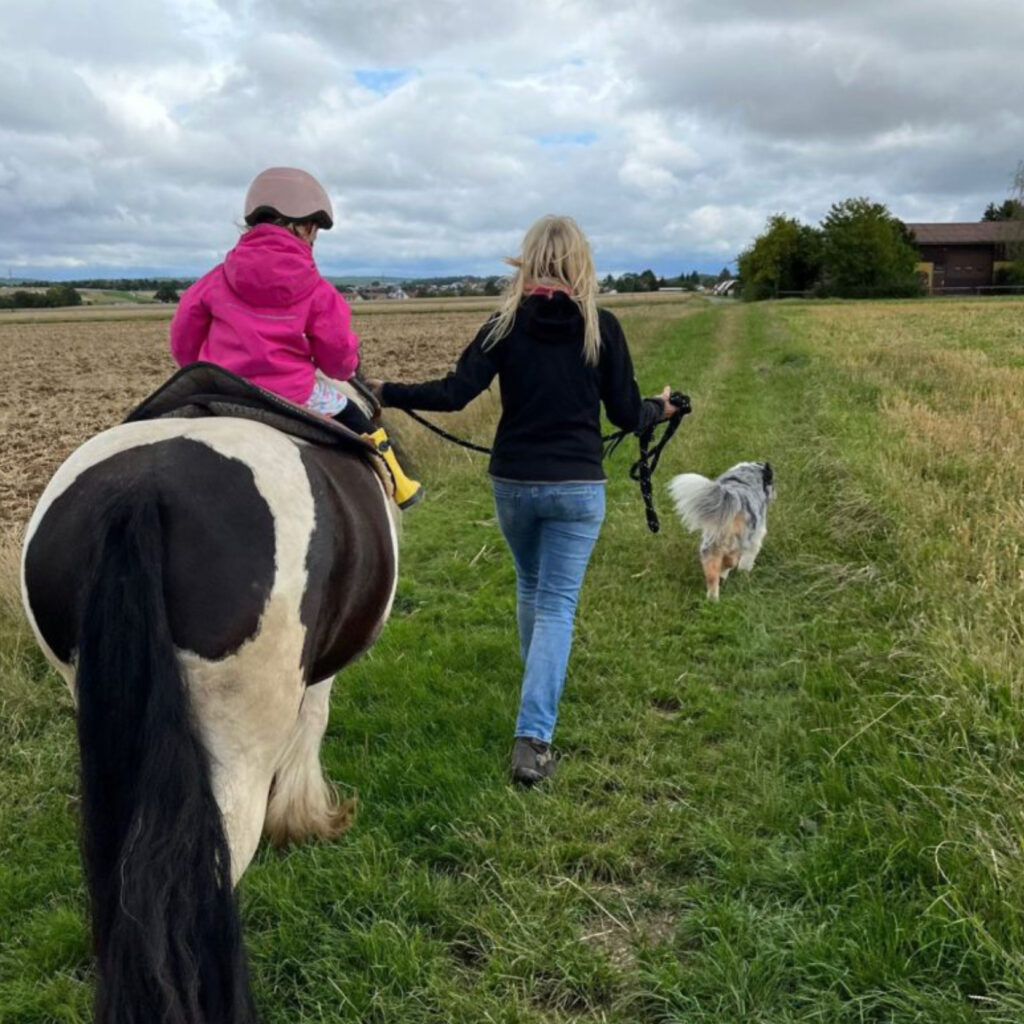 Reittherapeutin Gudrun Marquardt-Teuscher begleitet ein Kind auf Tinkerstute Lotti bei einem Spaziergang mit Hund Kibo.