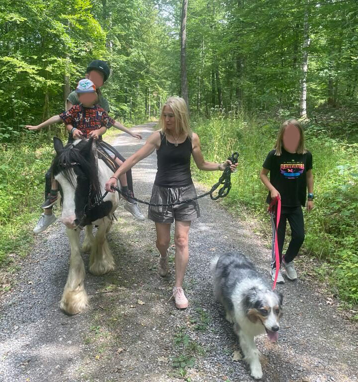Kinder und Erwachsene mit einem Tinkerpferd und Hund auf einem Waldweg